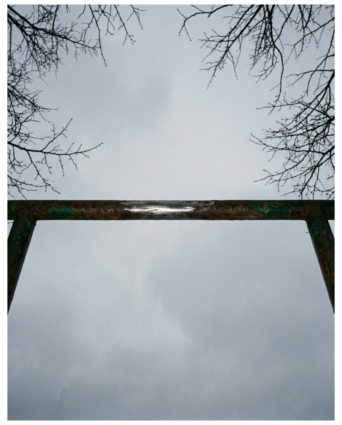 A weathered steel pull-up bar against an overcast sky