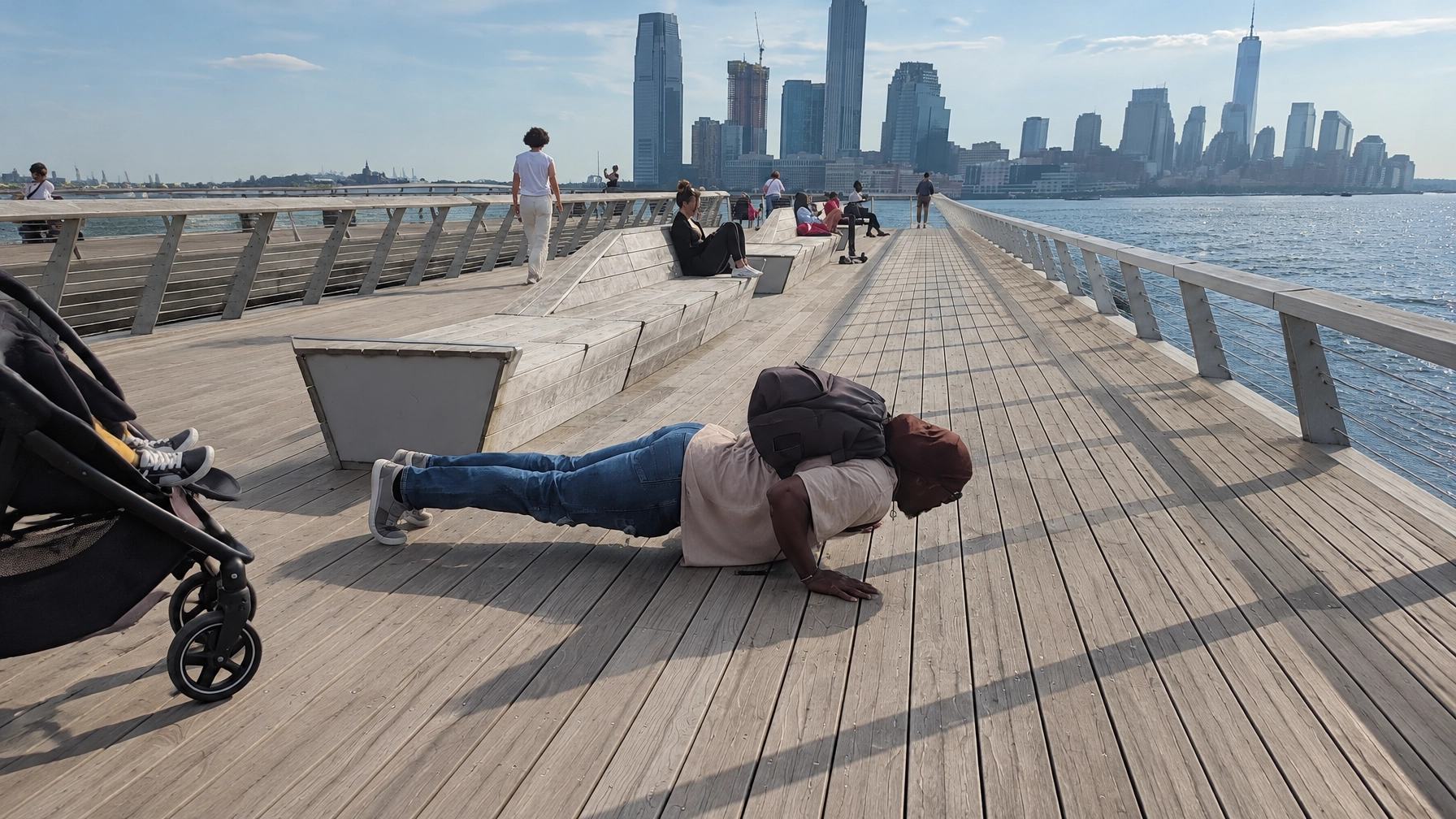 Irvin Charleston doing push-ups on a waterfront boardwalk with a weighted backpack, city skyline in the background